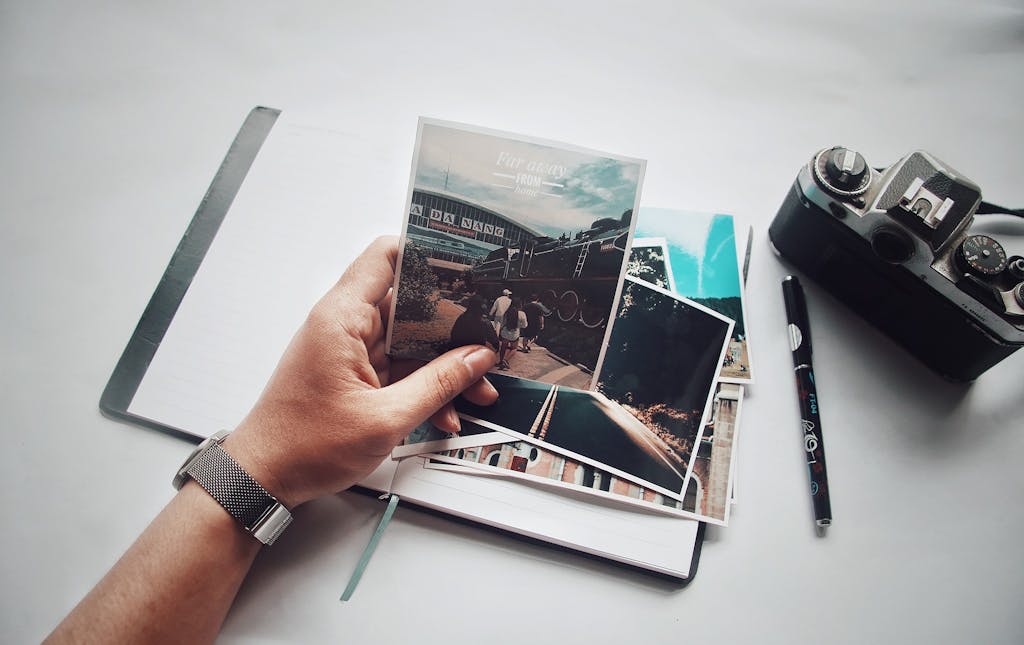 A person holding photos with a vintage camera and notebook on a desk.